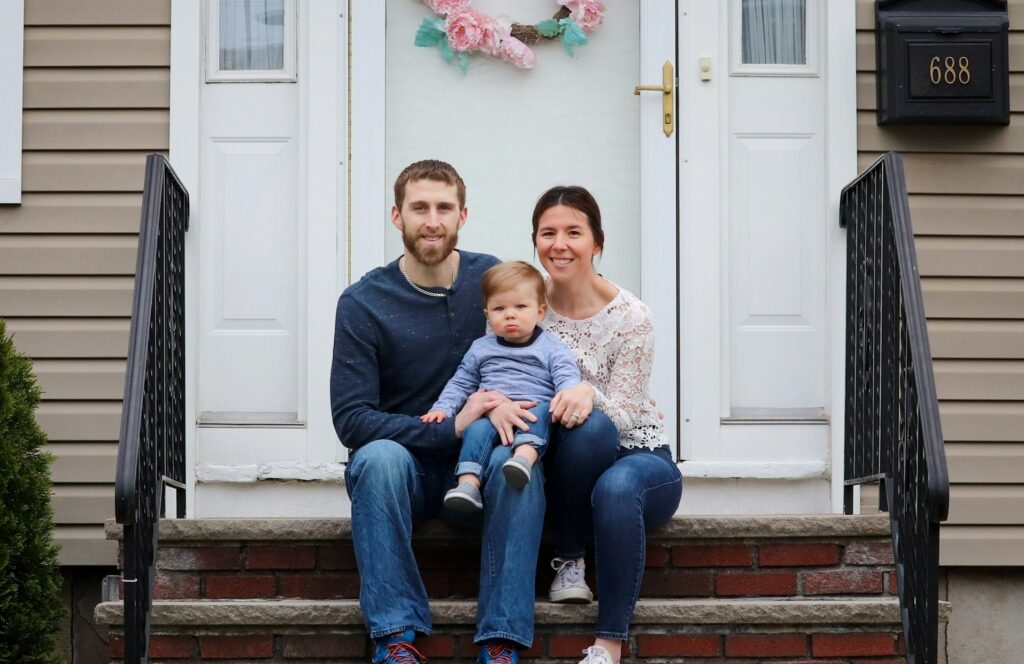 A man, woman, and young child sitting on the steps in front of a home