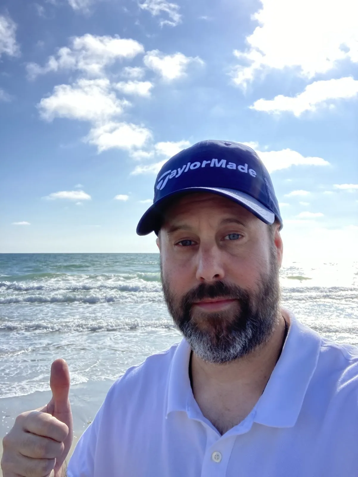 Man with hat making a thumbs up sign in front of the ocean