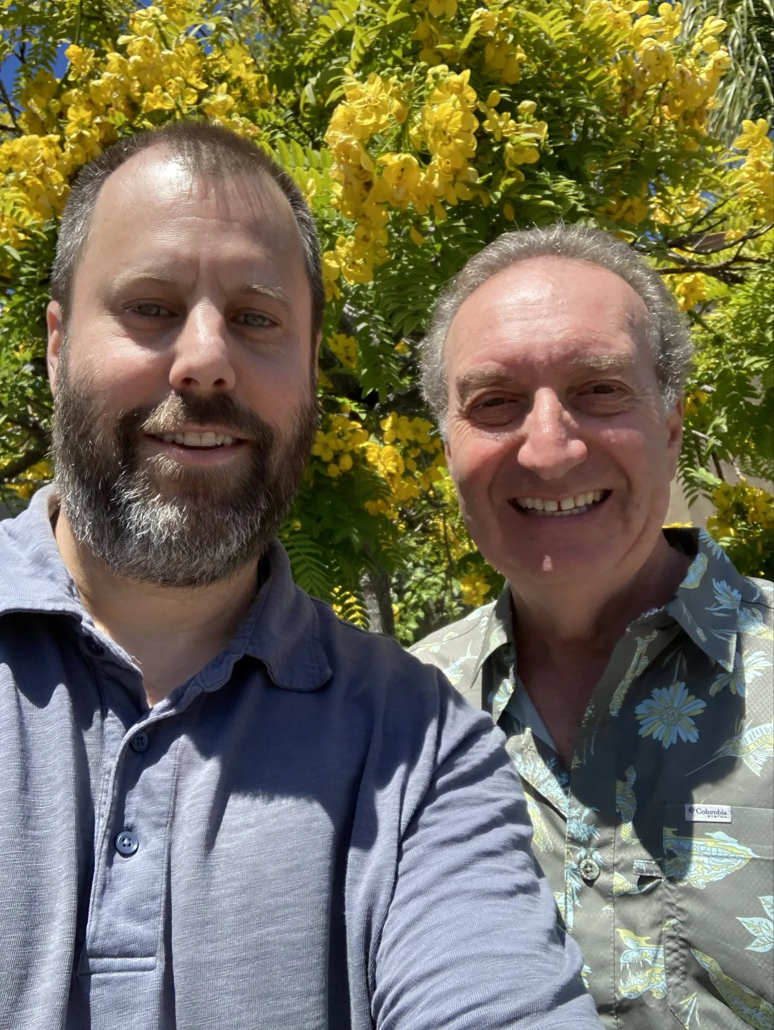 Two men smiling at the camera in front of a yellow floral tree