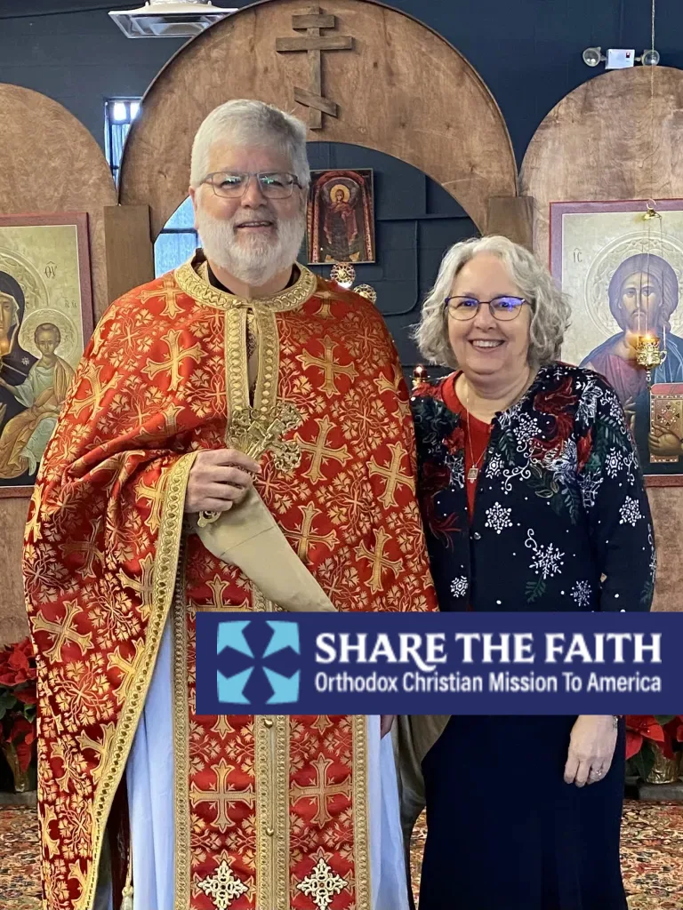 Fr. Andrew dressed in vestments and holding a cross and Kh Belinda in front of the iconostasis