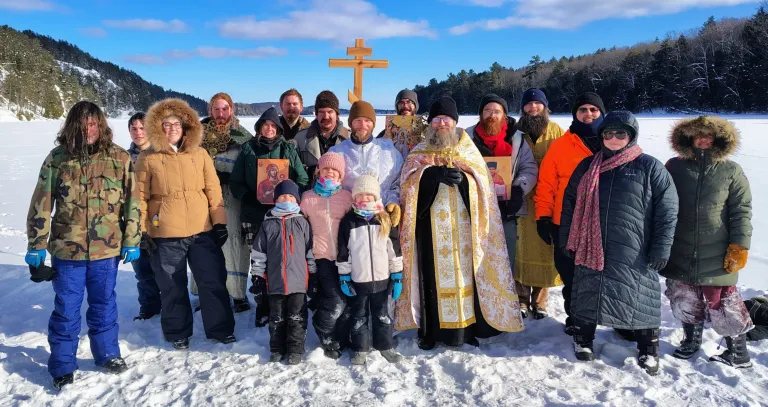 Priest holding cross and parish holding icons on snow and ice